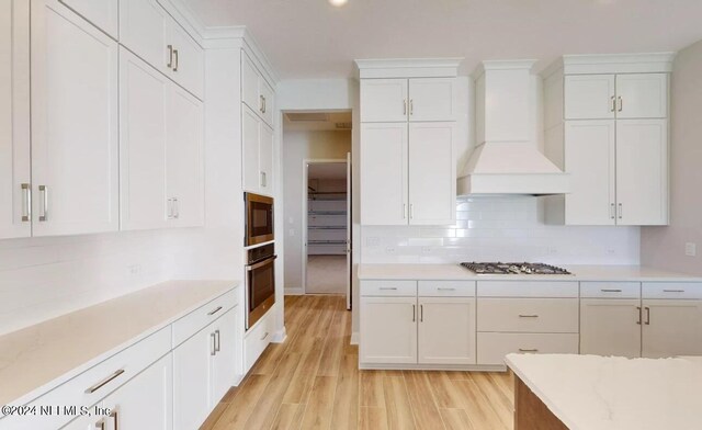 kitchen featuring white cabinetry, custom range hood, appliances with stainless steel finishes, and decorative backsplash