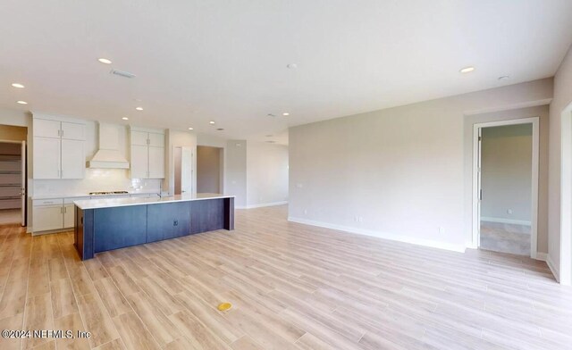 kitchen with light wood-style flooring, custom range hood, open floor plan, light countertops, and white cabinetry