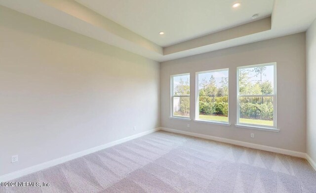 empty room featuring light carpet, a tray ceiling, recessed lighting, and baseboards