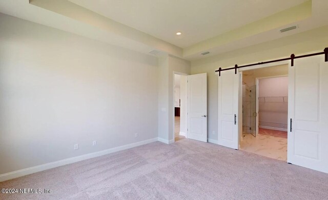 unfurnished bedroom with a barn door, recessed lighting, light carpet, visible vents, and baseboards