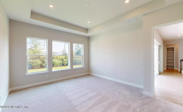 empty room featuring light colored carpet, baseboards, a raised ceiling, and recessed lighting