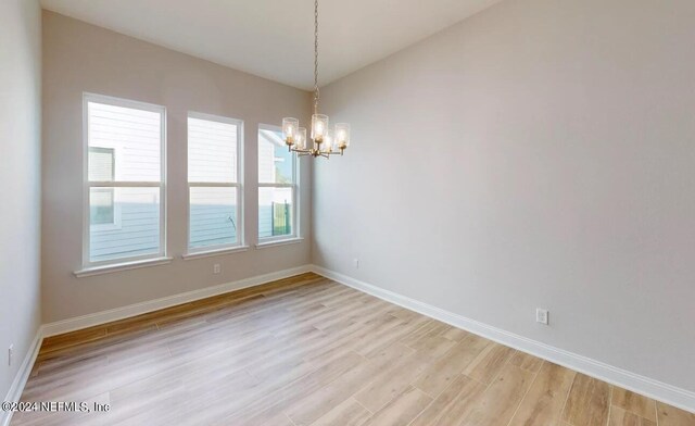 empty room featuring light wood-style floors, a chandelier, vaulted ceiling, and baseboards