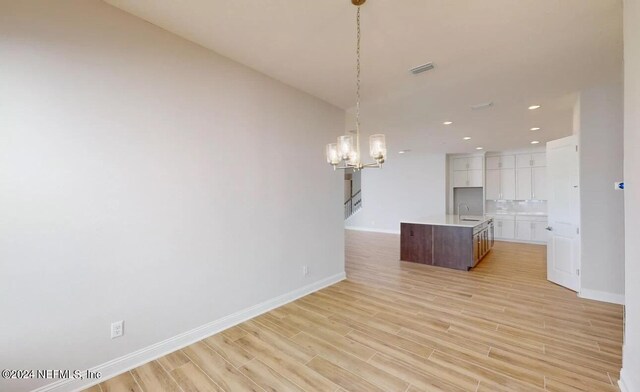 kitchen with visible vents, light wood-style flooring, white cabinetry, a sink, and an island with sink