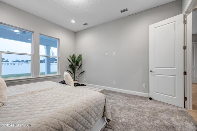 bedroom featuring a water view, light carpet, and a textured ceiling