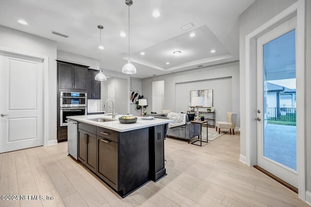 kitchen featuring appliances with stainless steel finishes, decorative light fixtures, sink, a center island with sink, and light wood-type flooring