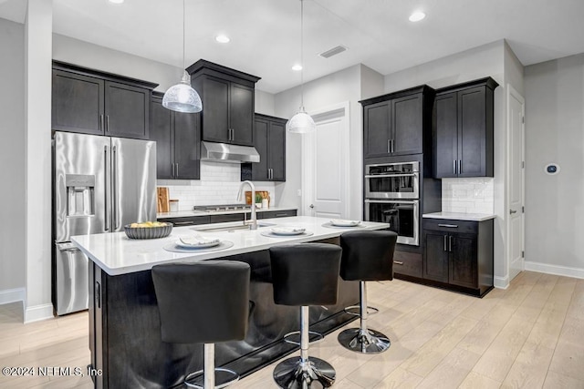 kitchen with a breakfast bar, pendant lighting, a kitchen island with sink, light hardwood / wood-style floors, and stainless steel appliances