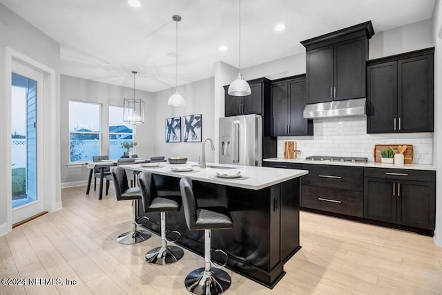 kitchen featuring a breakfast bar area, decorative light fixtures, a center island with sink, stainless steel appliances, and light hardwood / wood-style floors