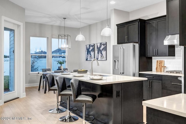 kitchen with pendant lighting, sink, high end refrigerator, and a center island with sink