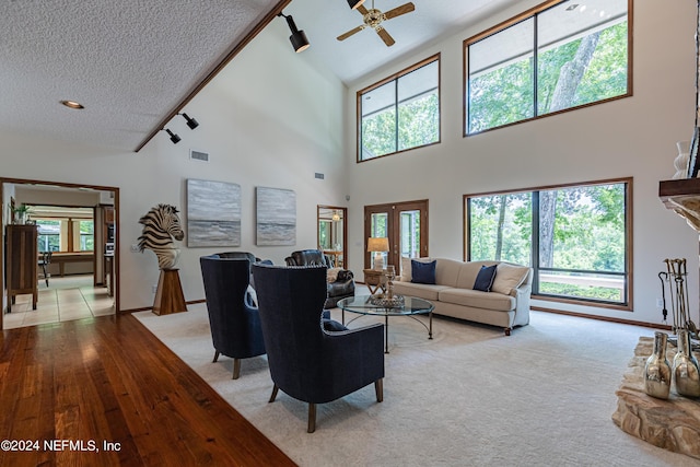 living room featuring ceiling fan, a high ceiling, a textured ceiling, and a stone fireplace