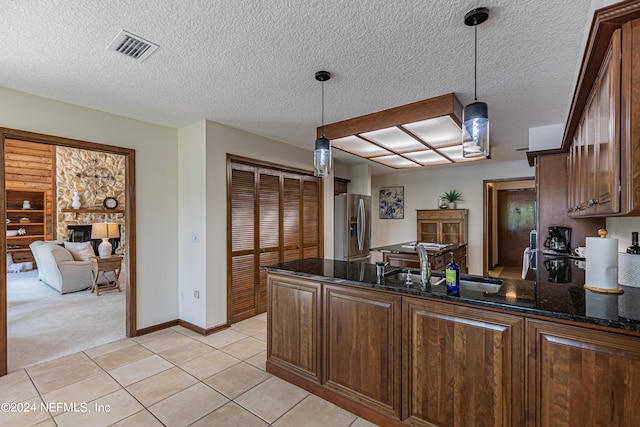 kitchen featuring a stone fireplace, stainless steel refrigerator with ice dispenser, dark stone counters, pendant lighting, and sink