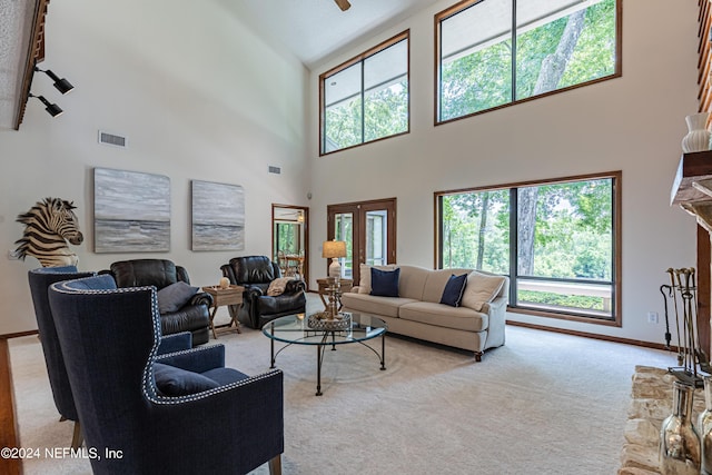 carpeted living room featuring a healthy amount of sunlight, french doors, a towering ceiling, and a stone fireplace