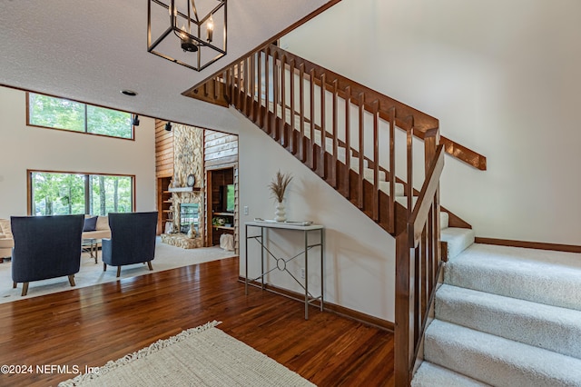 staircase with a towering ceiling, an inviting chandelier, a fireplace, and wood-type flooring