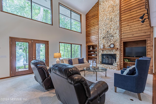 living room featuring light colored carpet, a towering ceiling, built in features, a stone fireplace, and french doors