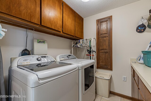 washroom with a textured ceiling, cabinets, light tile patterned flooring, and washer and clothes dryer