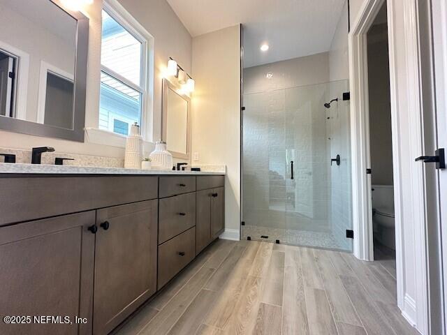 full bathroom with toilet, a sink, wood finished floors, a shower stall, and double vanity