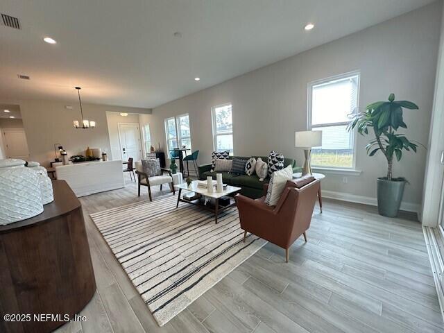 living area with visible vents, light wood finished floors, a healthy amount of sunlight, and an inviting chandelier