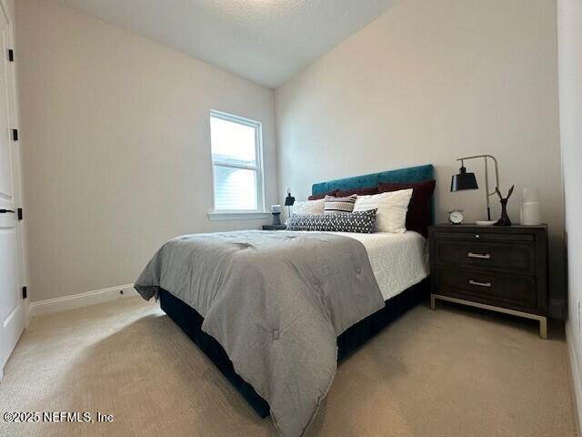 bedroom featuring lofted ceiling, light colored carpet, and baseboards