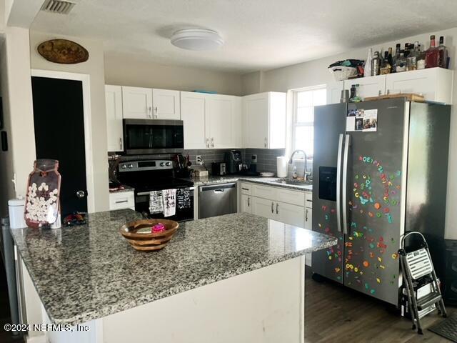 kitchen featuring kitchen peninsula, stainless steel appliances, white cabinets, stone counters, and sink