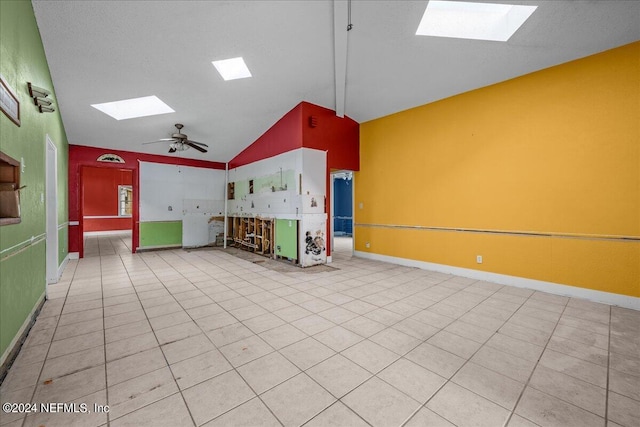 interior space featuring lofted ceiling with skylight, ceiling fan, light tile patterned floors, and baseboards