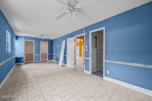 empty room with a ceiling fan, a textured ceiling, baseboards, and light tile patterned floors