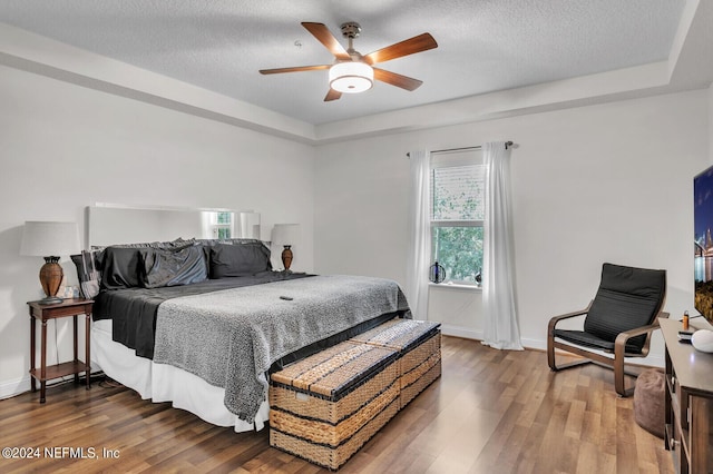 bedroom with a raised ceiling, wood-type flooring, and a textured ceiling