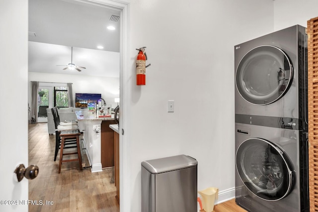 laundry room with stacked washer / drying machine, light hardwood / wood-style flooring, and ceiling fan