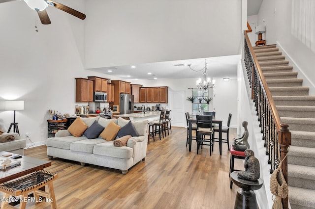 living room with a high ceiling, sink, ceiling fan with notable chandelier, and light wood-type flooring