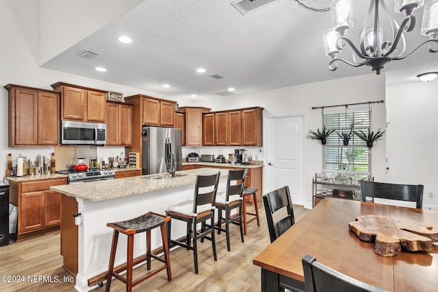 kitchen with stainless steel appliances, a breakfast bar area, light hardwood / wood-style floors, and a center island with sink