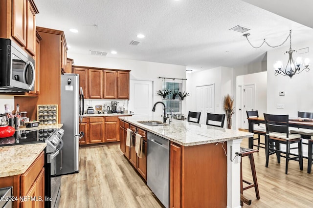 kitchen featuring sink, a kitchen breakfast bar, a kitchen island with sink, light stone counters, and stainless steel appliances