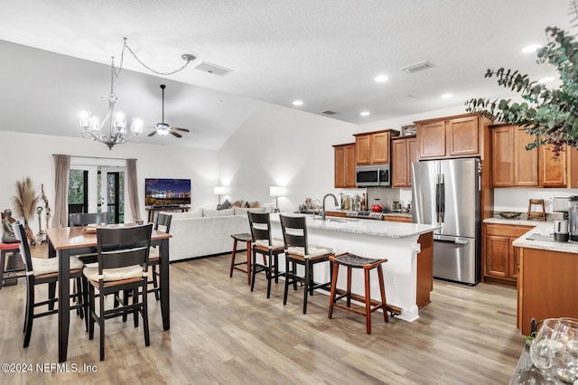 kitchen with stainless steel appliances, a kitchen island with sink, a breakfast bar area, and light hardwood / wood-style flooring