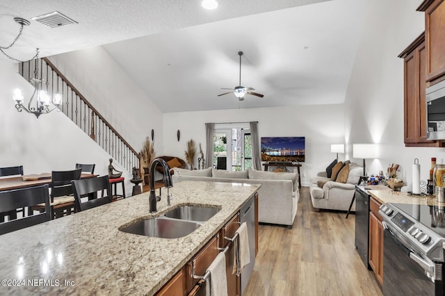 kitchen with sink, light stone counters, decorative light fixtures, light wood-type flooring, and stainless steel appliances