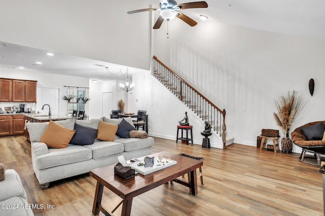 living room with ceiling fan with notable chandelier, sink, light hardwood / wood-style floors, and a high ceiling