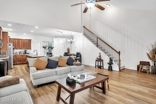 living room featuring sink, ceiling fan with notable chandelier, light wood-type flooring, and a towering ceiling