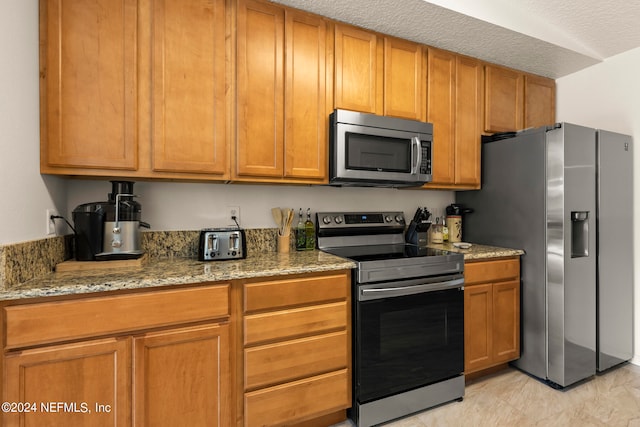 kitchen featuring light tile floors, appliances with stainless steel finishes, a textured ceiling, and light stone countertops