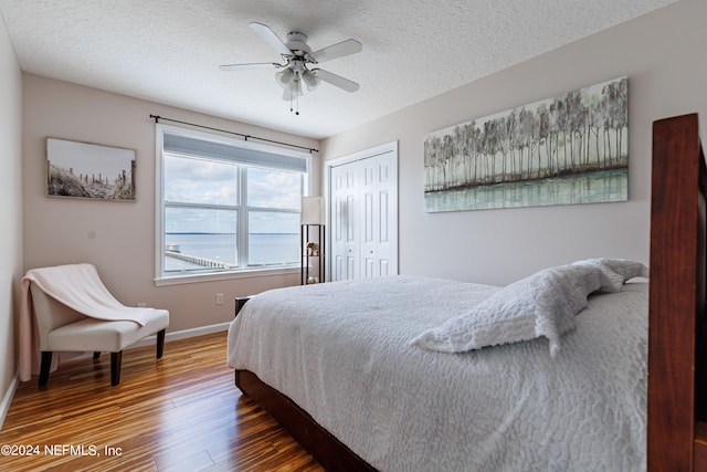 bedroom with dark wood-type flooring, ceiling fan, a closet, and a textured ceiling