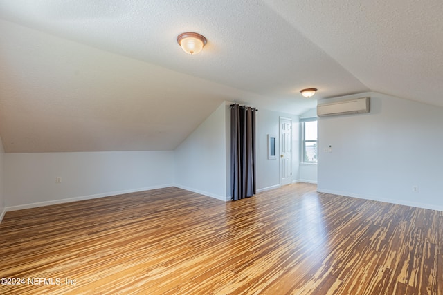 additional living space featuring hardwood / wood-style floors, vaulted ceiling, a wall unit AC, and a textured ceiling