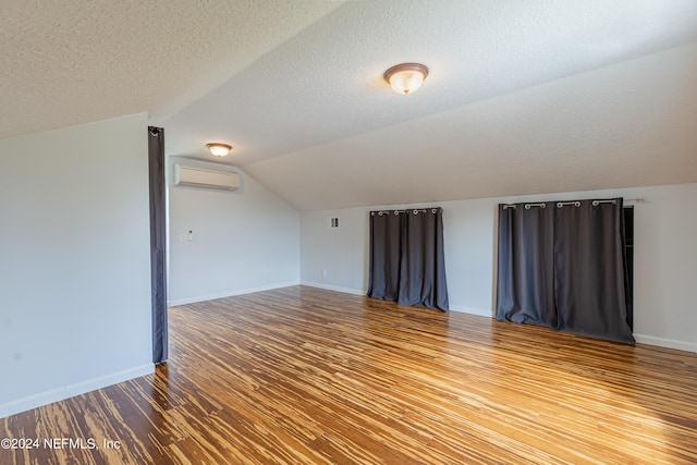 interior space featuring a textured ceiling, vaulted ceiling, a wall unit AC, and hardwood / wood-style flooring