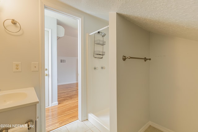 bathroom with wood-type flooring, vanity, walk in shower, and a textured ceiling