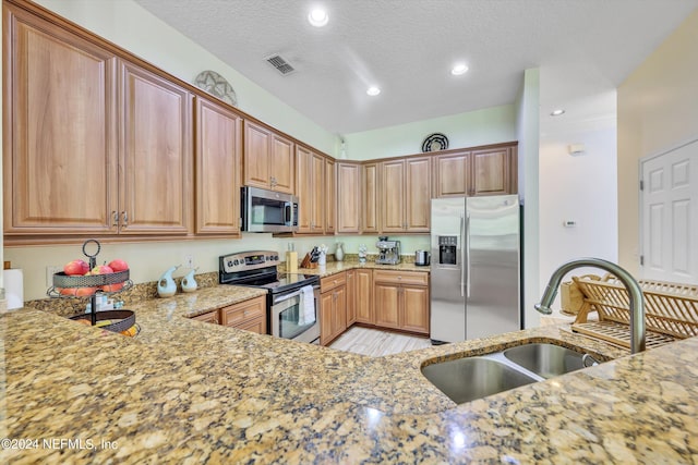 kitchen featuring a textured ceiling, stainless steel appliances, light stone counters, and sink