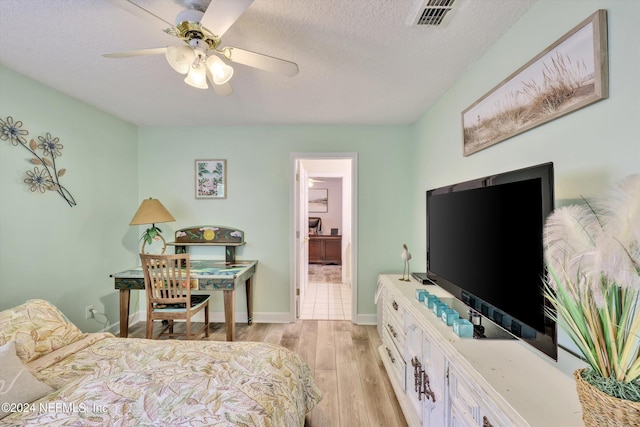 bedroom featuring a textured ceiling, ensuite bathroom, light hardwood / wood-style flooring, and ceiling fan