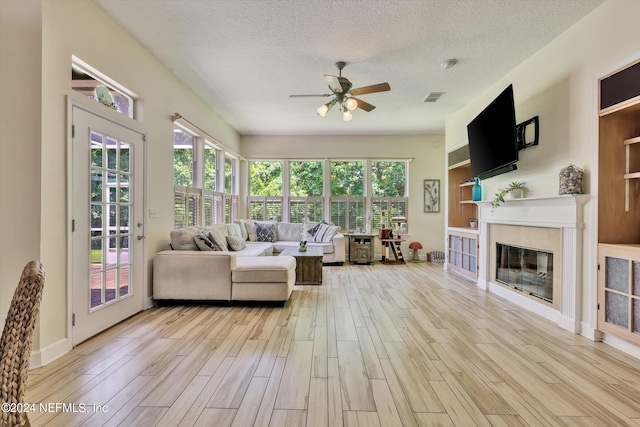 living room featuring ceiling fan, a healthy amount of sunlight, a textured ceiling, and light wood-type flooring