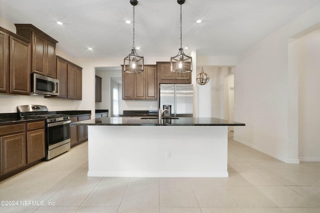 kitchen with appliances with stainless steel finishes, an island with sink, light tile floors, decorative light fixtures, and dark brown cabinetry