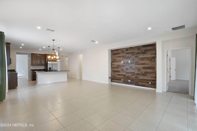 unfurnished living room with wooden walls, a notable chandelier, and light tile floors