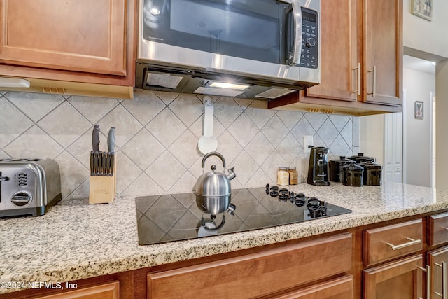 kitchen with black electric stovetop, backsplash, and light stone counters