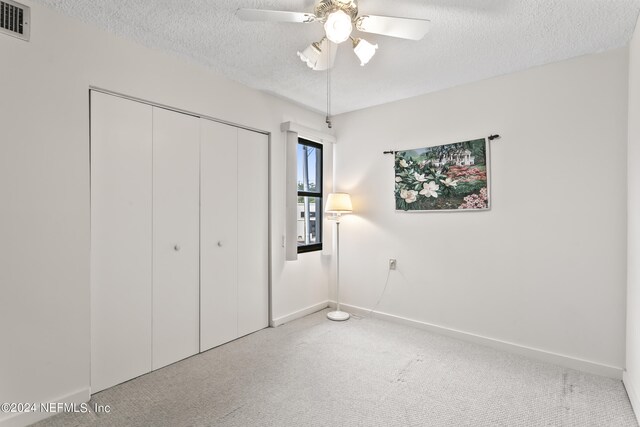 unfurnished bedroom featuring ceiling fan, a textured ceiling, a closet, and carpet