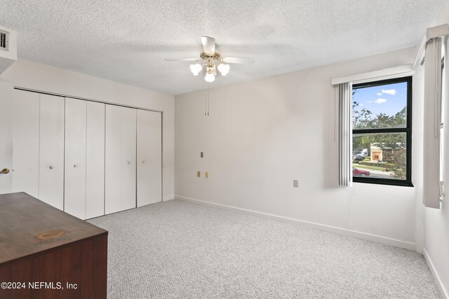 unfurnished bedroom with light carpet, a textured ceiling, a closet, and ceiling fan