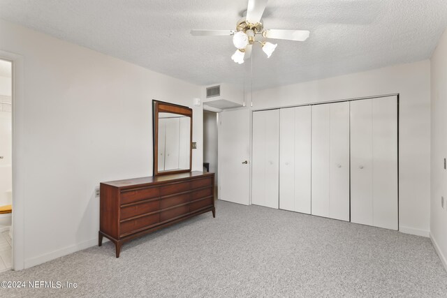 carpeted bedroom featuring ceiling fan, ensuite bath, a textured ceiling, and a closet