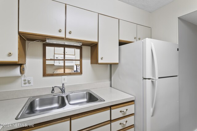 kitchen with sink, a textured ceiling, white fridge, and white cabinetry