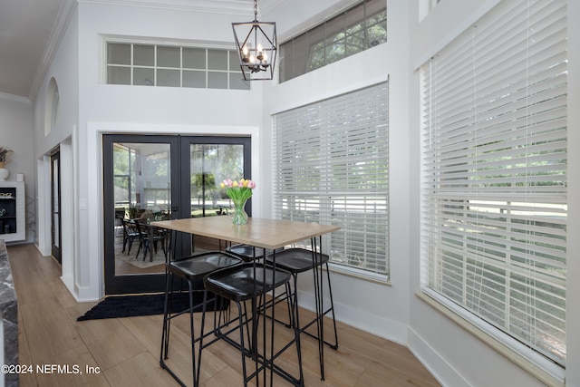 dining space featuring french doors, ornamental molding, a chandelier, a high ceiling, and light wood-type flooring