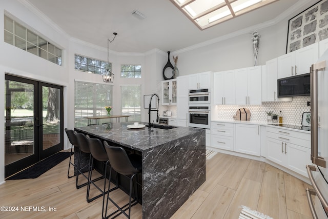 kitchen with tasteful backsplash, white cabinets, black appliances, a kitchen island with sink, and sink